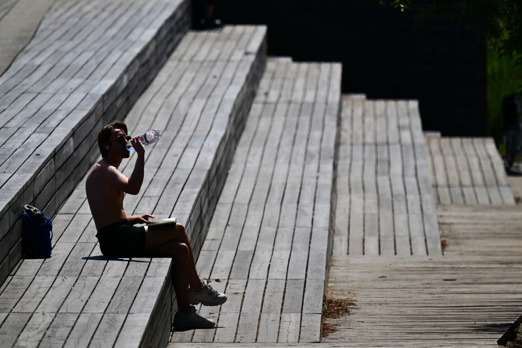 A man is sitting in the sun in the park at Gleisdreieck, Berlin, drinking water, Tuesday, June 23, 2026, (Sebastian Gollnow/dpa via AP)