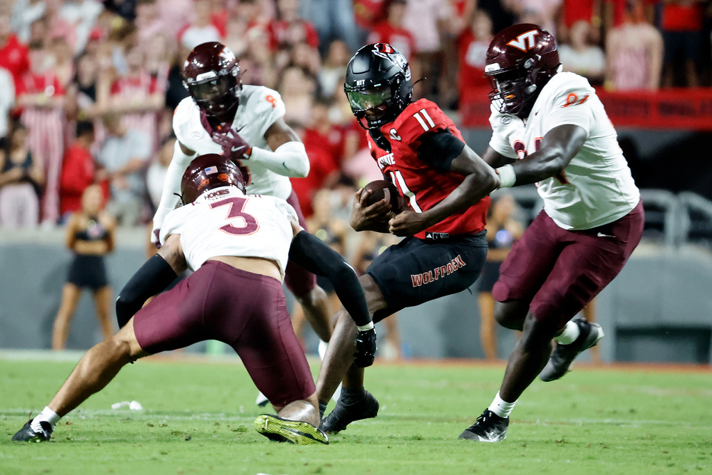 North Carolina State quarterback CJ Bailey (11) is surrounded by Virginia Tech linebacker Kaleb Spencer (3), defensive lineman Elhadj Fall (94) and Christian Ellis (8) during the first half of an NCAA college football game in Raleigh, N.C., Saturday, Sept. 27, 2025. (AP Photo/Karl DeBlaker)