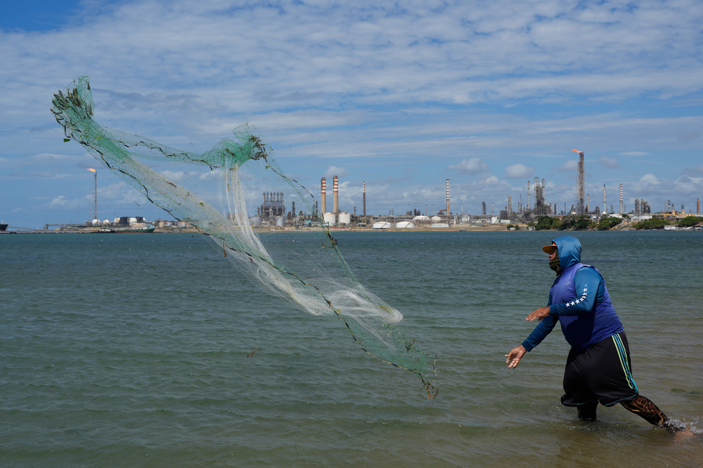A fisherman throws his net with the Cardon refinery in the background in Punta Cardon, Venezuela, Wednesday, Jan. 14, 2026. (AP Photo/Matias Delacroix)