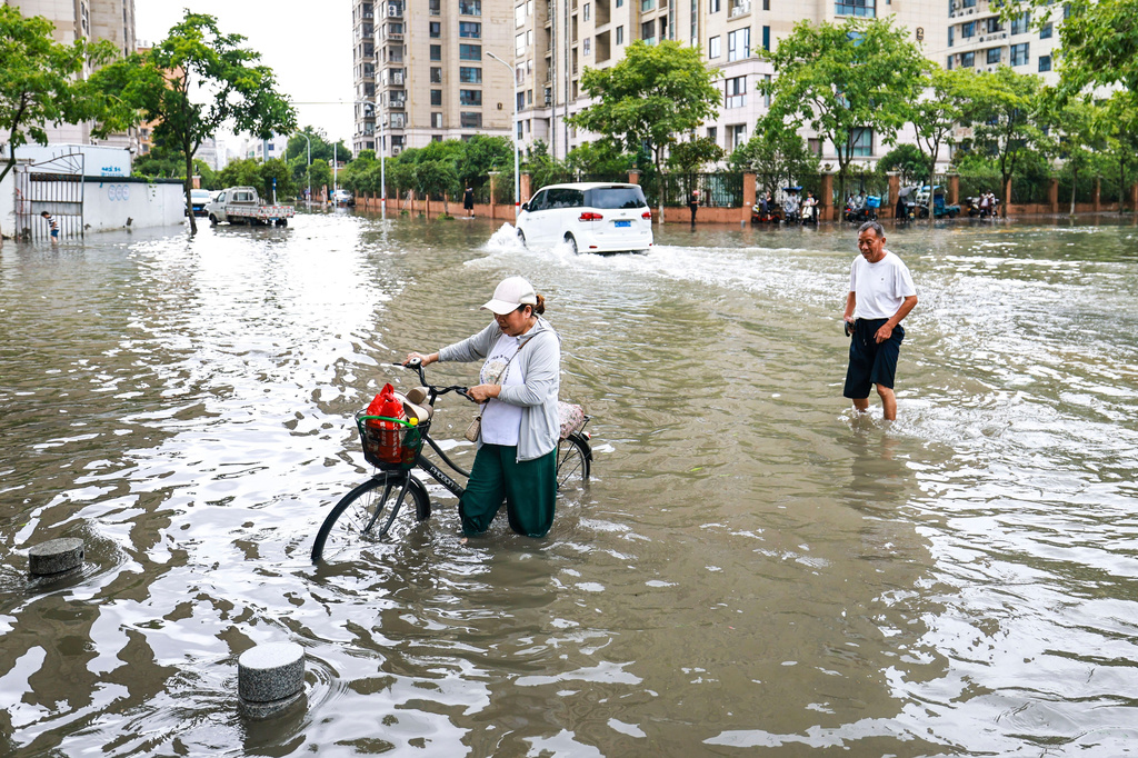 In this photo released by Xinhua News Agency, residents try to get through a flooded road in the aftermath of Typhoon Bavi in Yueqing City, eastern China's Zhejiang Province, July 12, 2026. (Jiang Han/Xinhua via AP)