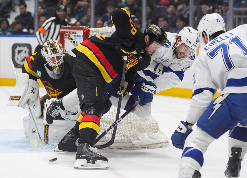 Tampa Bay Lightning's Brandon Hagel, back right, passes the puck while being checked by Vancouver Canucks' Marcus Pettersson (29) as Canucks goalie Kevin Lankinen, left, watches during the first period of an NHL hockey game in Vancouver, British Columbia, Thursday, March 19, 2026. (Darryl Dyck/The Canadian Press via AP)