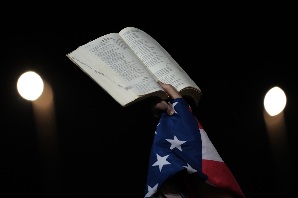 A supporter of former President Jair Bolsonaro holds a Bible and the American flag during a vigil in his support near his home where he is under house arrest, in Brasilia, Brazil, Wednesday, Sept. 10, 2025. (AP Photo/Eraldo Peres)