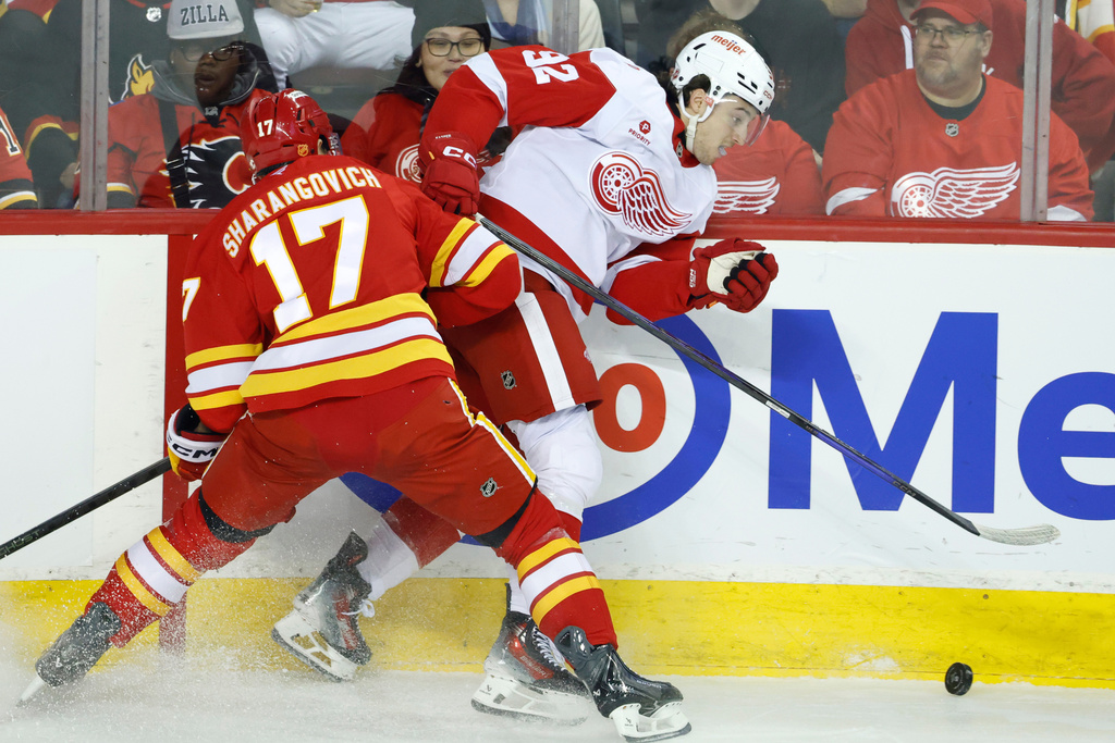 Detroit Red Wings' Marco Kasper (32) takes a hit from Calgary Flames' Yegor Sharangovich (17) during the first period of an NHL hockey game in Calgary, Alberta, on Wednesday, Dec. 10, 2025. (Larry MacDougal/The Canadian Press via AP)