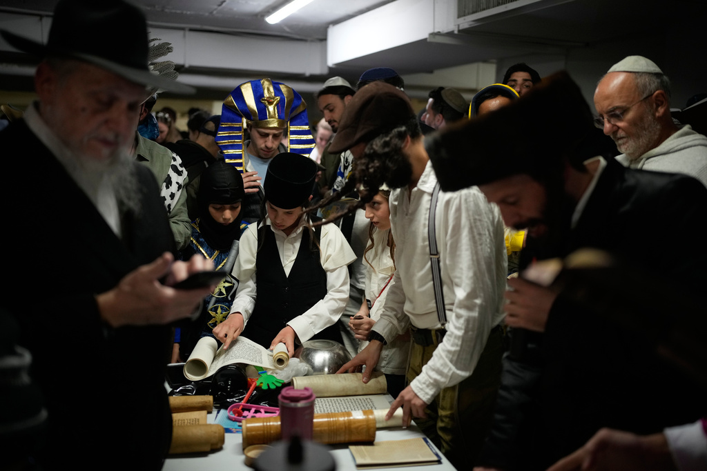 Jewish men and children, some dressed in costumes, read the Scroll of Esther as they celebrate the holiday of Purim in an underground parking garage as a precaution against possible Iranian missile attacks, in Tel Aviv, Israel, Monday, March 2, 2026. (AP Photo/Ohad Zwigenberg)