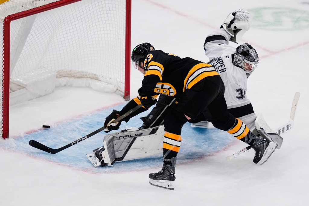 Boston Bruins defenseman Charlie McAvoy, left, scores the game-winner off Los Angeles Kings goaltender Darcy Kuemper, right, during an overtime period of an NHL hockey game, Tuesday, March 10, 2026, in Boston. (AP Photo/Charles Krupa)