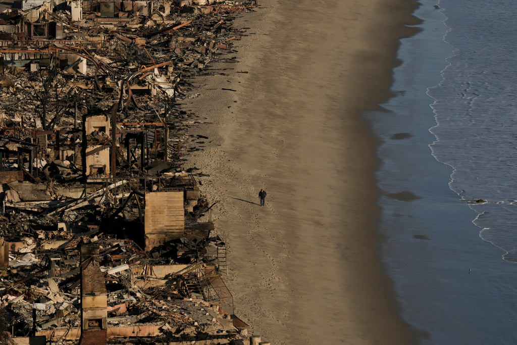 FILE - A person walks on the beach next to homes damaged by the Palisades Fire on Jan. 16, 2025, in Malibu, Calif. (AP Photo/Jae C. Hong, File)