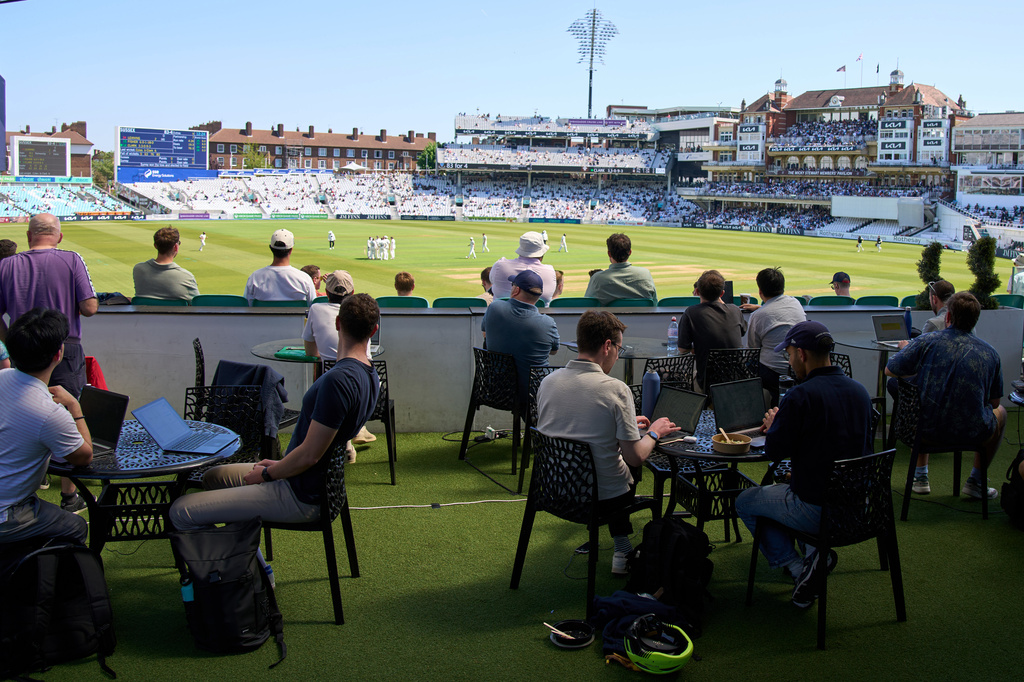 People work and watch cricket during a Surrey against Sussex County Championship cricket match at the Kia Oval in London, Friday, May 1, 2026. (AP Photo/Tony Hicks)