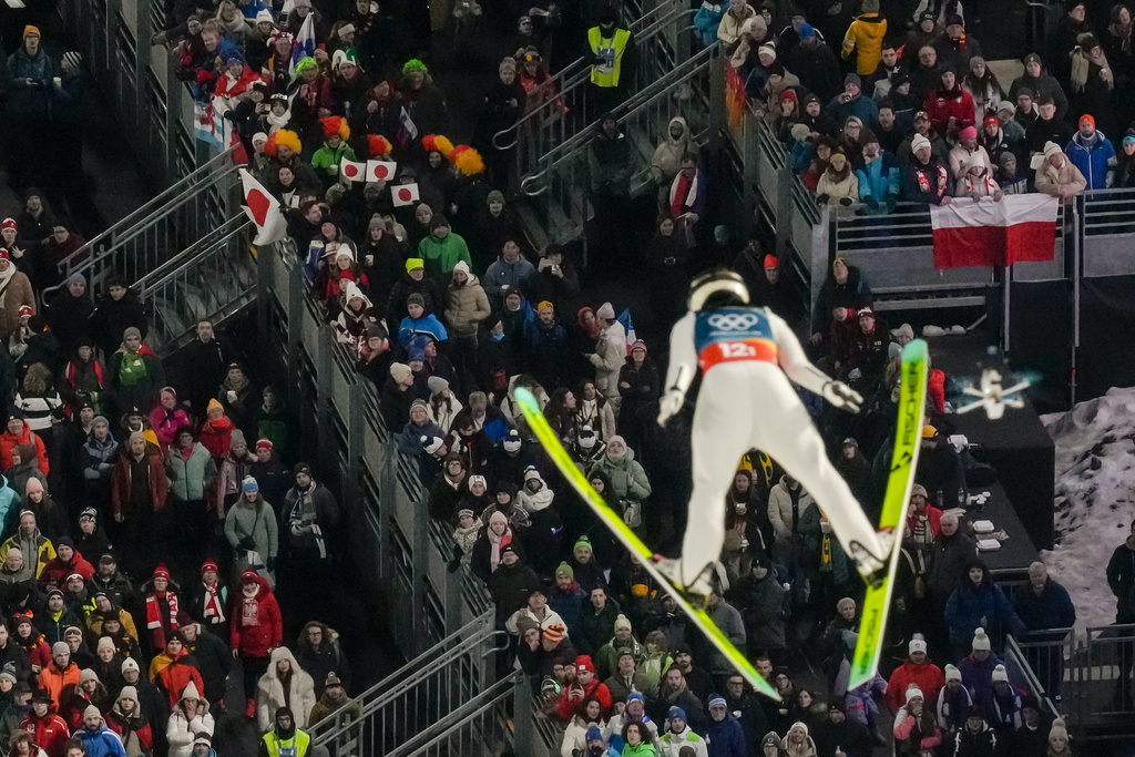 Fans watch Nozomi Maruyama, of Japan, soaring through the air during the ski jumping mixed team competition at the 2026 Winter Olympics, in Predazzo, Italy, Tuesday, Feb. 10, 2026.(AP Photo/Evgeniy Maloletka)