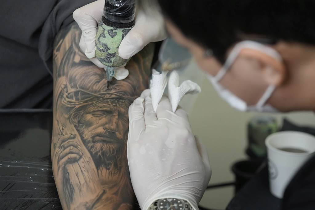 Tattoo artist Song Jaemin, right, works to tattoo an image of Jesus Christ on the forearm of Lee Byong-joo at his studio in Goyang, South Korea, Thursday, Sept. 18, 2025. (AP Photo/Ahn Young-joon)