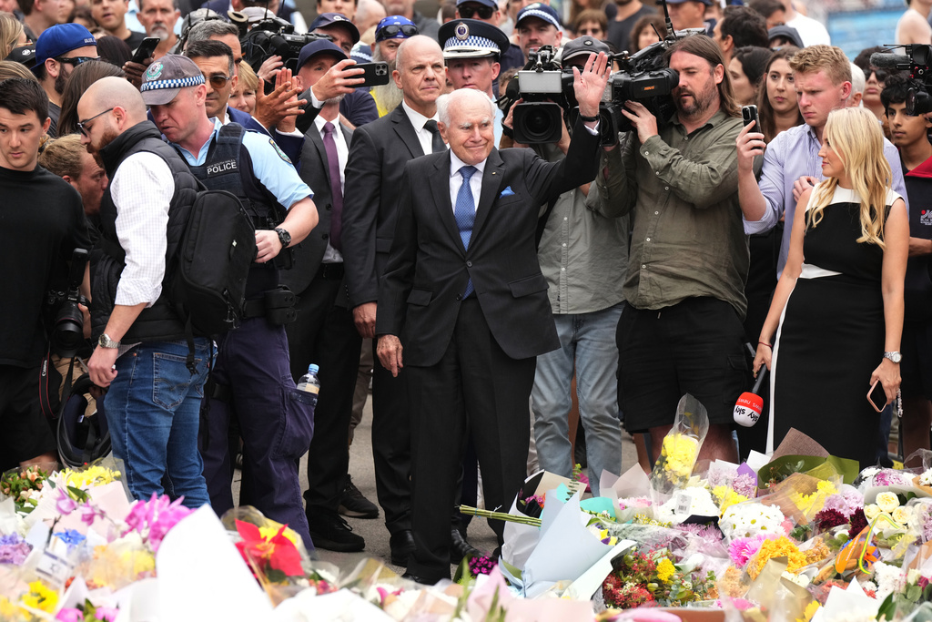 Former PM John Howard waves during a flower memorial for victims of Sunday's shooting at the Bondi Pavilion at Bondi Beach on Tuesday, Dec. 16, 2025, in Sydney, Australia. (AP Photo/Mark Baker)