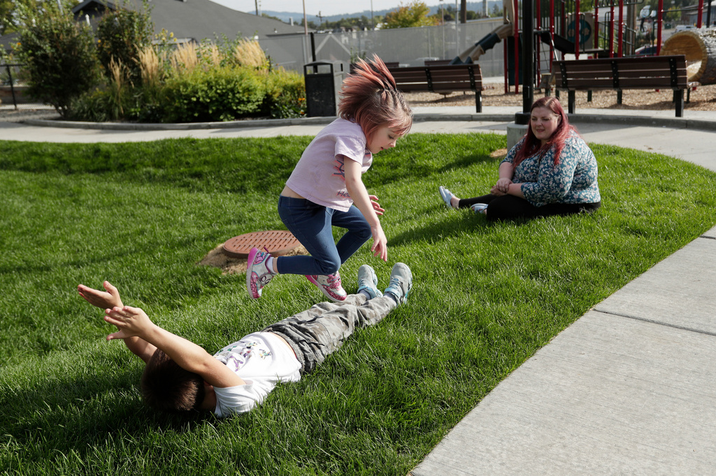Evie Reed, center, jumps over her brother Kian Reed, left, as her mother Cassie Reed watches outside their apartment building, Tuesday, Sept. 22, 2026, in Spokane, Wash. (AP Photo/Young Kwak)