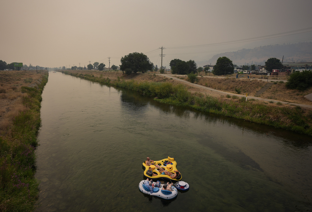 People float on the Channel Pathway that connects Okanagan Lake and Skaha Lake as smoke from wildfires burning in the region fills the air, in Penticton, British Columbia, Monday, Aug. 10, 2026. (Darryl Dyck/The Canadian Press via AP)