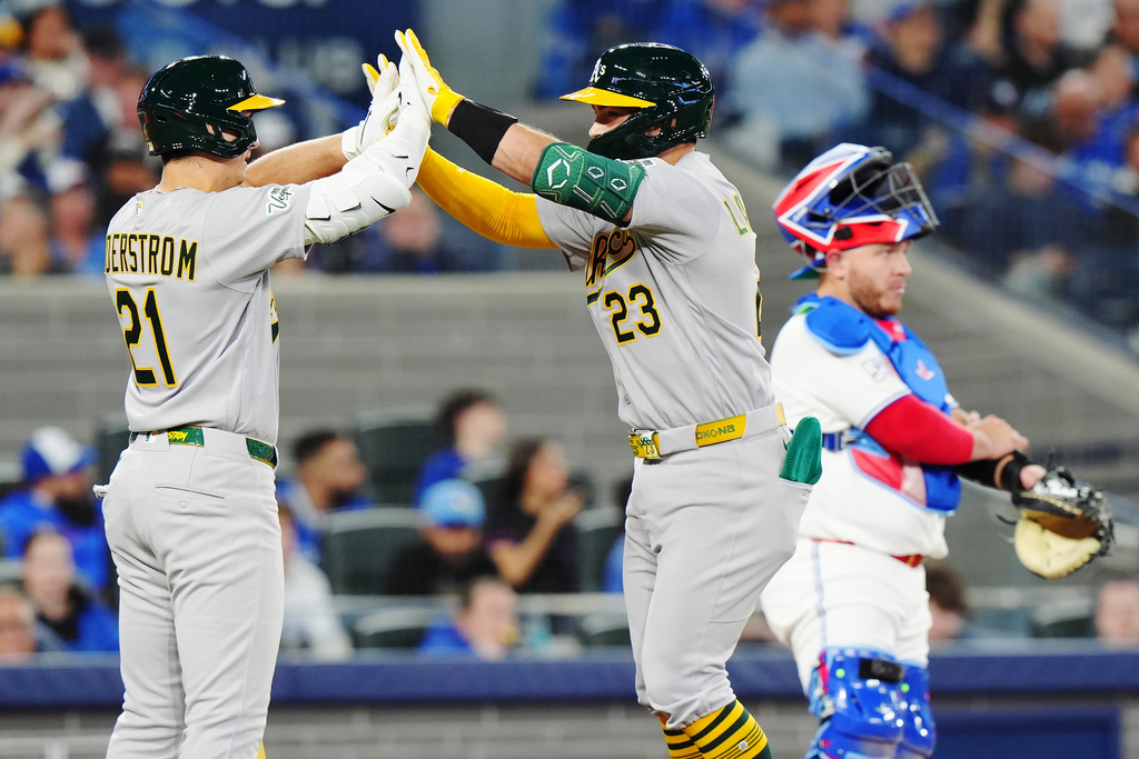 Athletics' Shea Langeliers (23) celebrates his solo home run with Tyler Soderstrom (21) as Toronto Blue Jays catcher Alejandro Kirk (right) looks on during the fourth inning of a baseball game in Toronto on Friday, March 27, 2026. (Nathan Denette/The Canadian Press via AP)