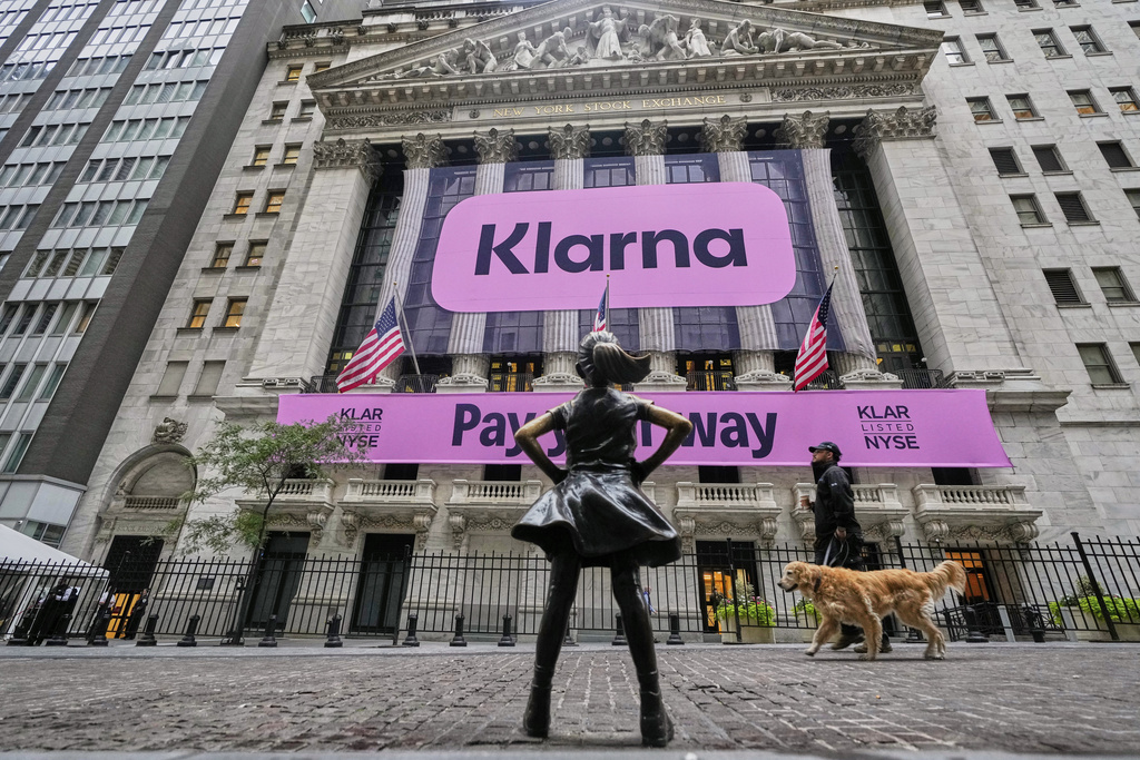 The Fearless Girl statue faces the facade of the New York Stock Exchange that displays signage for Sweden's Klarna, Wednesday, Sept. 10, 2025. (AP Photo/Richard Drew)