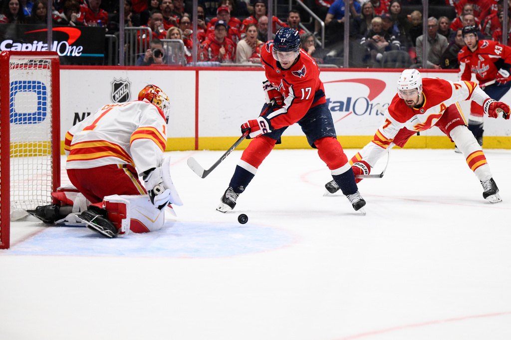 Washington Capitals center Dylan Strome (17) tries to get the puck past Calgary Flames goaltender Devin Cooley (1) and defenseman Kevin Bahl (7) during the first period of an NHL hockey game, Monday, March 9, 2026, in Washington. (AP Photo/Nick Wass)