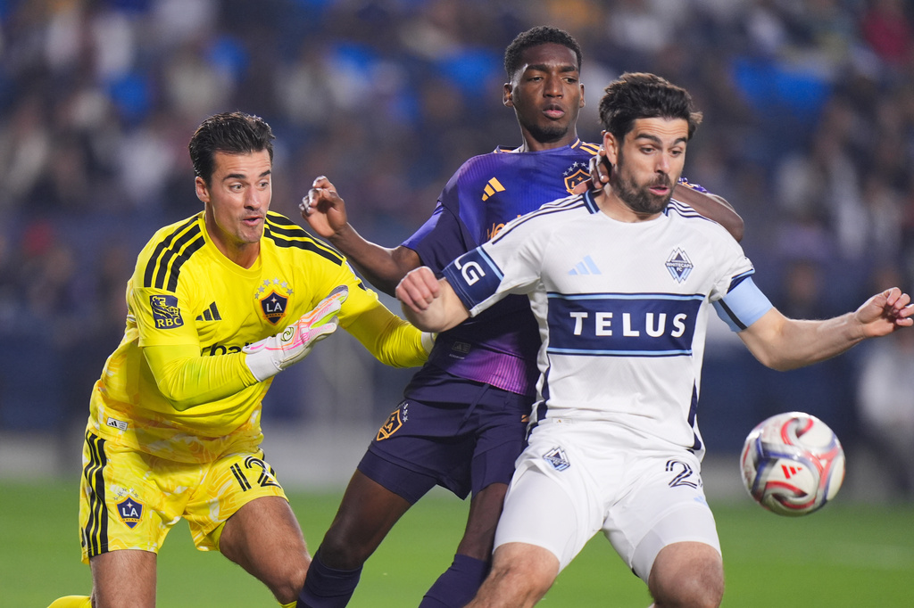 Los Angeles Galaxy goalkeeper James Marcinkowski (12) watches as defender Emiro Garces, center, and Vancouver Whitecaps forward Brian White fight for the ball during the first half of an MLS soccer match Saturday, May 2, 2026, in Carson, Calif. (AP Photo/Jae C. Hong)