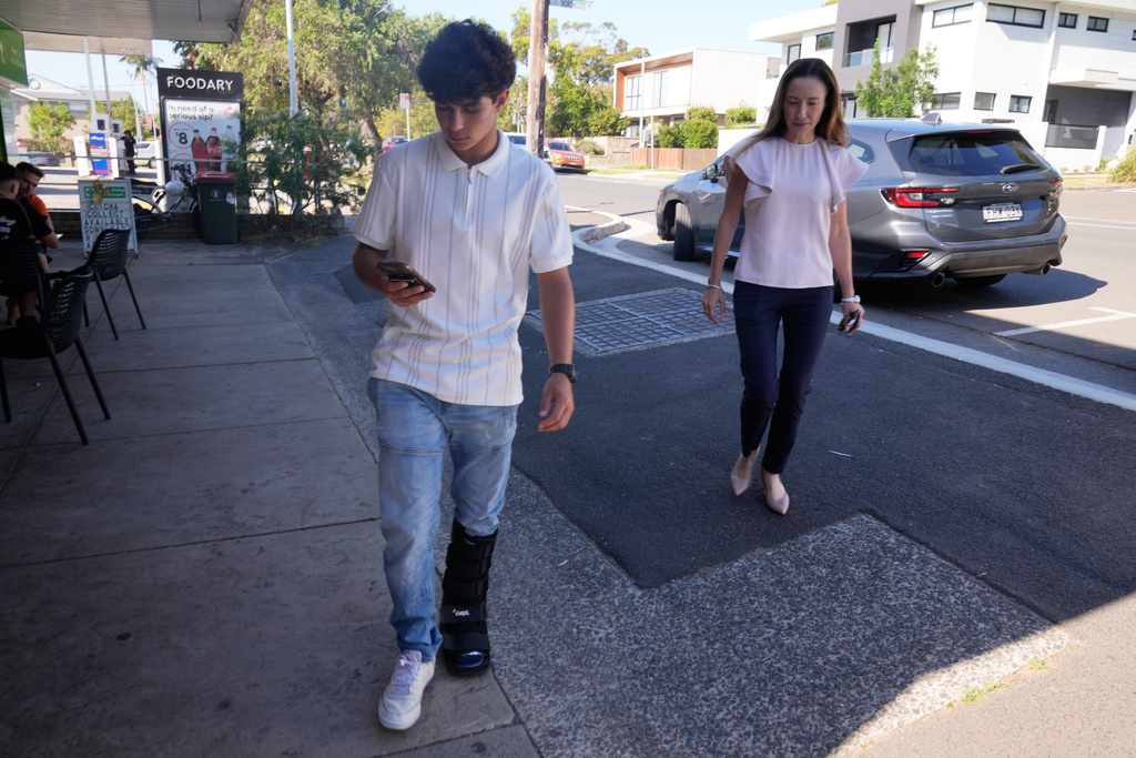Noah Jones, left, uses his phone as his mother Renee, walks toward him in Sydney, Tuesday, Dec. 9, 2025. (AP Photo/Rick Rycroft)