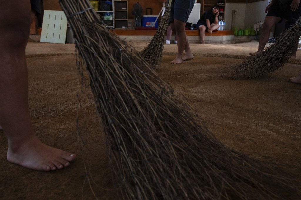 Wrestlers sweep the clay ring with brooms during a practice session at a sumo camp in Tottori Johoku High School in Tottori, Japan, on July 28, 2025. (AP Photo/Louise Delmotte)