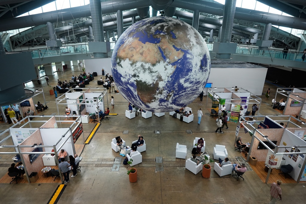 Attendees sit under a globe in a lobby at the side events pavilions at the COP30 U.N. Climate Summit, Tuesday, Nov. 11, 2025, in Belem, Brazil. (AP Photo/Fernando Llano)