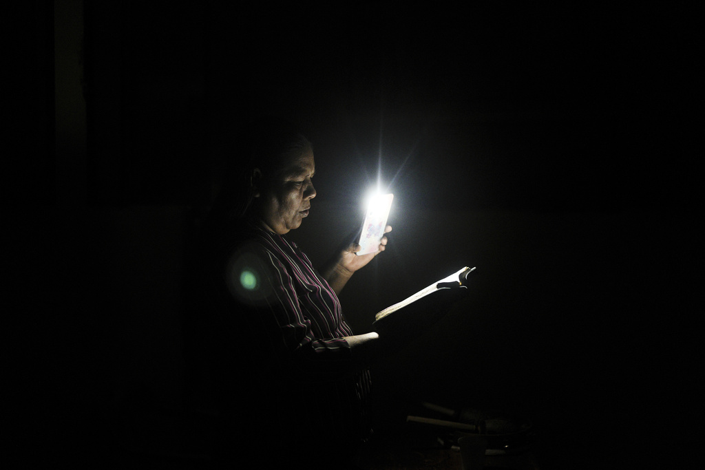A woman illuminates her Bible with a flashlight during a power outage in an evangelical church in Santa Rosa, Peru, an island on the Amazon River at the triple border with Colombia and Brazil, Sunday, Aug. 17, 2025. (AP Photo/Ivan Valencia)