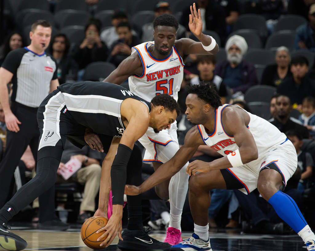 San Antonio Spurs center Victor Wembanyama, left, tangles with New York Knicks players Mohamed Diawara and OG Anunoby during the first half of an NBA basketball game, Wednesday, Dec. 31, 2025, in San Antonio. (AP Photo/Darren Abate)