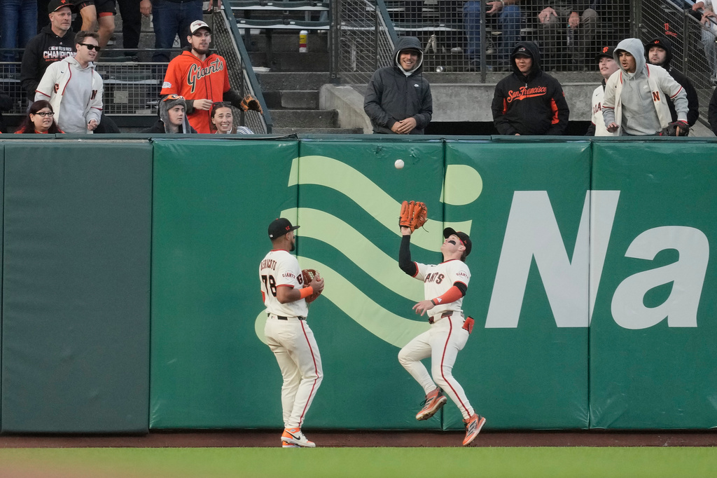 San Francisco Giants left fielder Victor Bericoto, left, watches as center fielder Drew Gilbert, right, catches a fly out hit by Colorado Rockies' Kyle Karros during the fifth inning of a baseball game Thursday, July 9, 2026, in San Francisco. (AP Photo/Jeff Chiu)