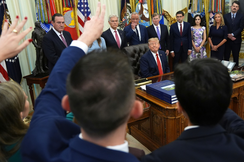 Reporters raise their hands to ask a question as President Donald Trump, seated, listens during an event about healthcare in the Oval Office of the White House, Friday Sept. 18, 2026, in Washington. (AP Photo/Jacquelyn Martin)