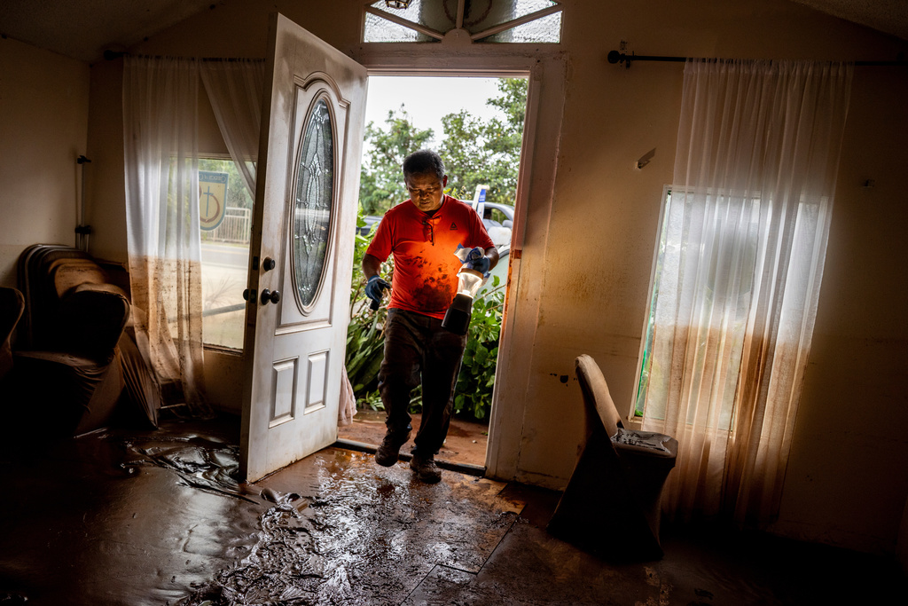 Glenn Duquez, associate pastor at the Church of God Jesus is Alive Fellowship, carries a lamp into the mud-riddled church building to clean up after the fast-moving flood in Haleiwa, Hawaii Saturday, March 21, 2026. (Stephen Lam/San Francisco Chronicle via AP)