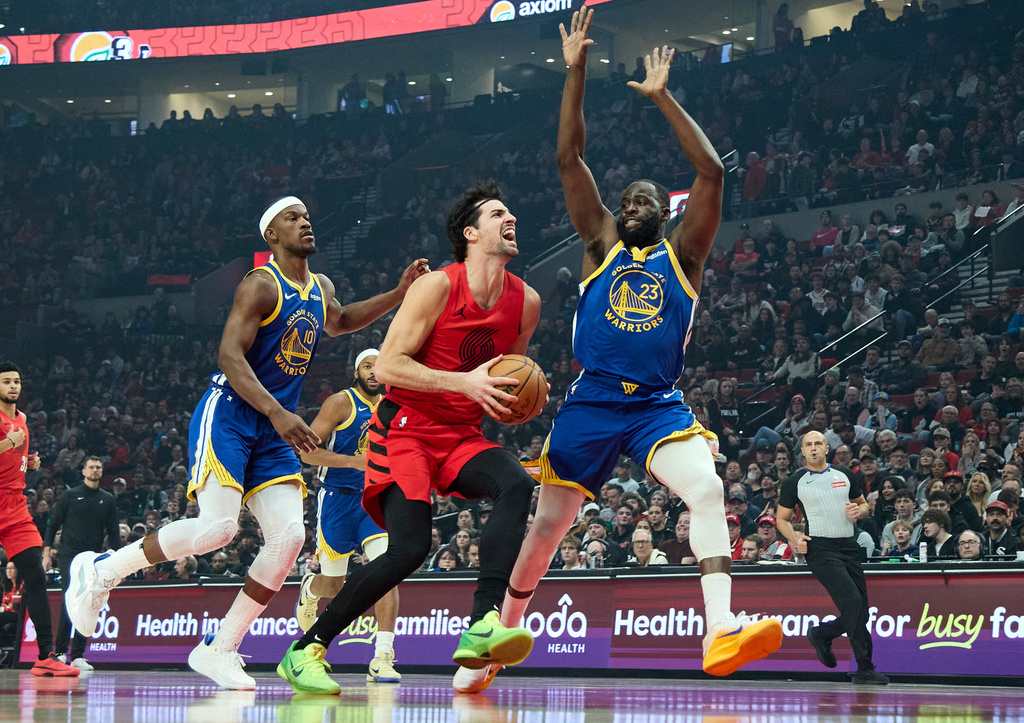 Portland Trail Blazers forward Deni Avdija, center, drives to the basket between Golden State Warriors forwards Jimmy Butler III, left, and Draymond Green (23) during the first half of an NBA basketball game in Portland, Ore., Sunday, Dec. 14, 2025. (AP Photo/Craig Mitchelldyer)