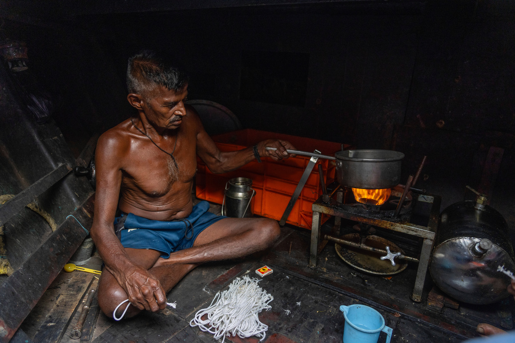 A fisherman prepares tea on a stove in a boat anchored due the price high at Sassoon Dock in Mumbai, India, Tuesday, April 7, 2026. (AP Photo/Rafiq Maqbool)