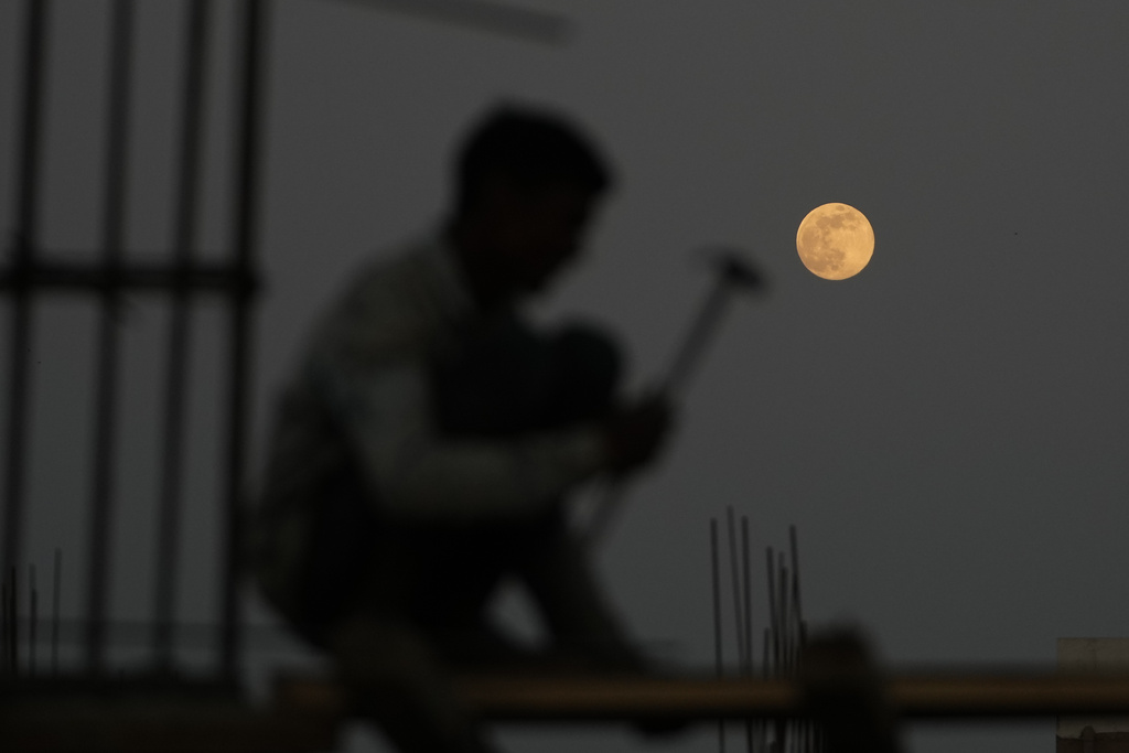 A laborer works at a construction site as a supermoon rises in Ahmedabad, India, Thursday, Dec. 4, 2025. (AP Photo/Ajit Solanki)