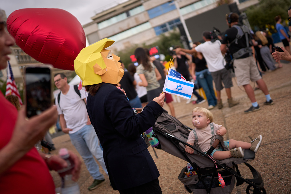 A child watches at a person wearing a mask depicting U.S. President Donald Trump as relatives and supporters of Israeli hostages held by Hamas in the Gaza Strip celebrate following the announcement that Israel and Hamas have agreed to the first phase of a peace plan to pause the fighting, as they gather at a plaza known as hostages square in Tel Aviv, Israel, Thursday, Oct. 9, 2025. (AP Photo/Emilio Morenatti)
