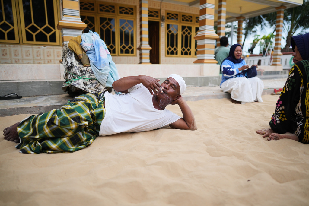 Adnan, who goes by one name only, smokes a cigarette as he lies on sand in Legung Timur village in Sumenep on Madura Island, Indonesia, Tuesday, Sept. 9, 2025. (AP Photo/Dita Alangkara)
