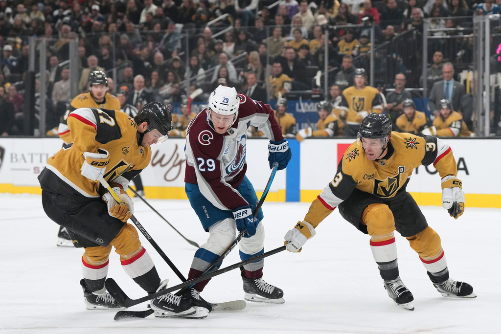 Colorado Avalanche center Nathan MacKinnon (29) skates with the puck against Vegas Golden Knights defensemen Ben Hutton, left, and Brayden McNabb (3) during the first period of an NHL hockey game, Saturday, Dec. 27, 2025, in Las Vegas. (AP Photo/Candice Ward)
