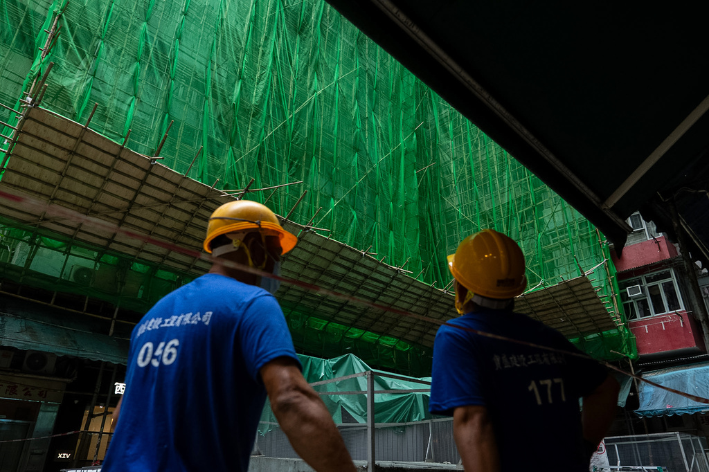Construction workers stand nearby a building under renovations in Quarry Bay district after the deadly fire at Wang Fuk Court, in the Tai Po district of Hong Kong's New Territories, Thursday, Dec 4, 2025. (AP Photo/Chan Long Hei)