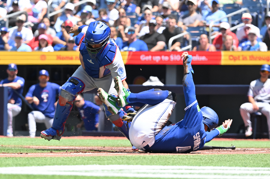 Toronto Blue Jays designated hitter George Springer, right, is tagged out at home by Texas Rangers catcher Elias Diaz, left, during the first inning of a baseball game in Toronto, Sunday, June 28, 2026. (Jon Blacker/The Canadian Press via AP)