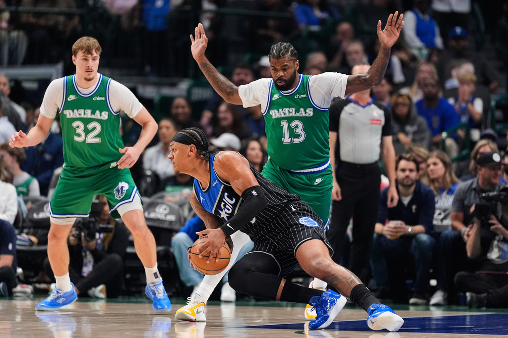 Orlando Magic forward Paolo Banchero, bottom, loses his footing as he works against Dallas Mavericks' Naji Marshall (13) in the first half of an NBA basketball game Friday, April 3, 2026, in Dallas. (AP Photo/Tony Gutierrez)