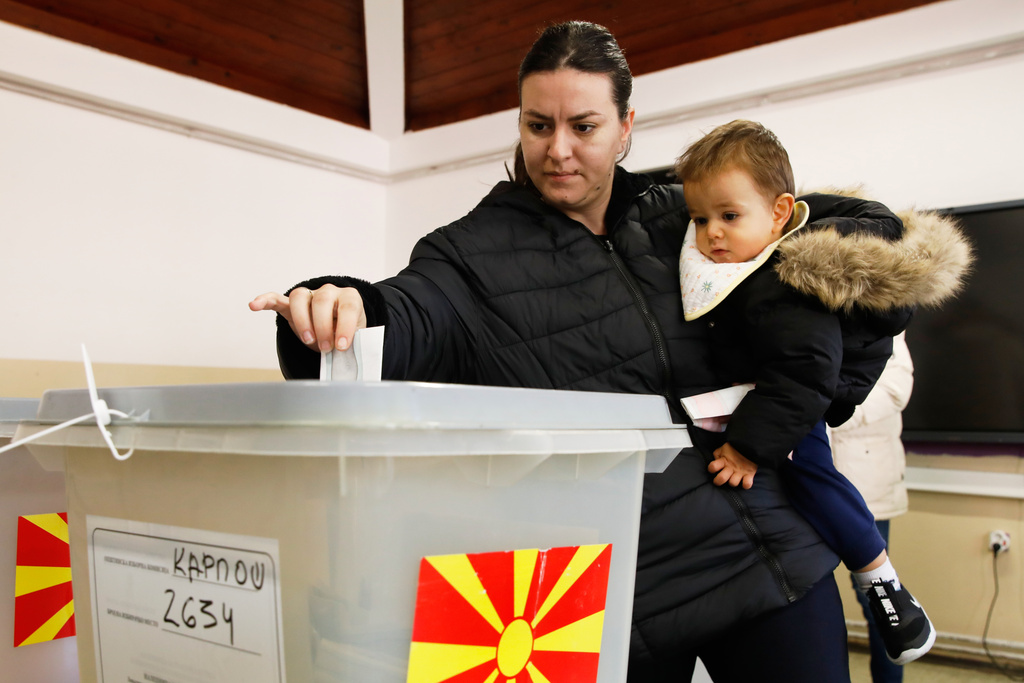 A woman holding a baby casts her ballot in the runoff local elections, at a polling station in Skopje, North Macedonia, on Sunday, Nov. 2, 2025. (AP Photo/Boris Grdanoski)