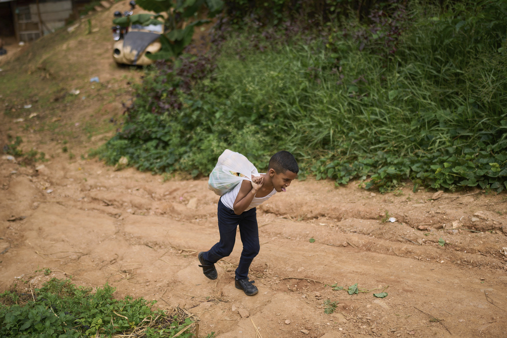 A youth carries groceries to a church-run soup kitchen that provides weekday lunches for schoolchildren in La Vega, on the outskirts of Caracas, Venezuela, Wednesday, July 2, 2025. (AP Photo/Ariana Cubillos)