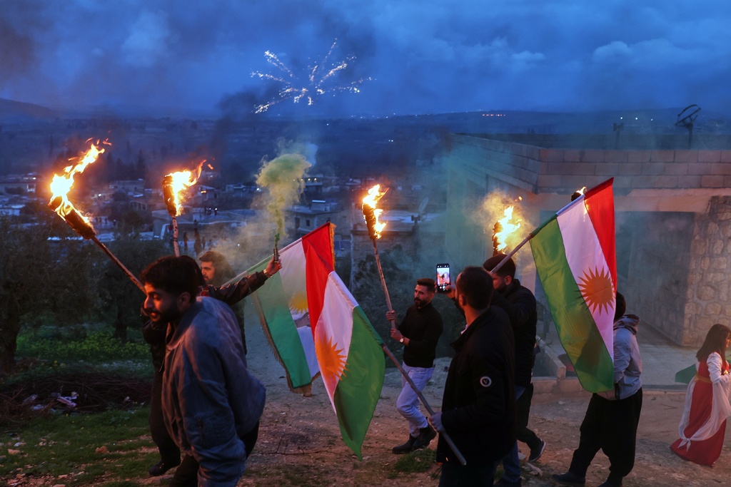 Syrian Kurds hold lit torches and Kurdish flags as they celebrate Nowruz, the Persian New Year, in the village of Basuta in the Afrin countryside, Syria, Friday, March 20, 2026. (AP Photo/Ghaith Alsayed)