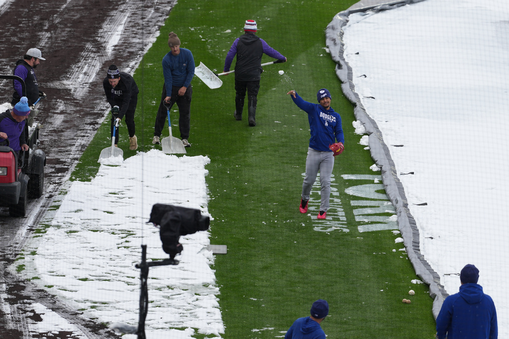 As the grounds crew works around him, Los Angeles Dodgers third baseman Santiago Espinal tosses a snowball at a coach while warming up to face the Colorado Rockies in a baseball game after a spring storm blanketed the intermountain West with a light covering of snow Friday, April 17, 2026, in Denver. (AP Photo/David Zalubowski)