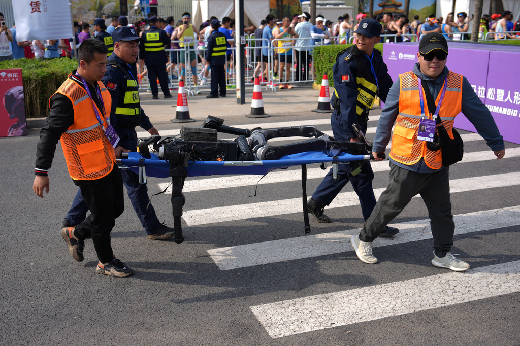 Security personnel and participants use a stretcher to carry a robot after it competed in the Beijing E-Town Half Marathon and Humanoid Robot Half-Marathon on the outskirts of Beijing, Sunday, April 19, 2026. (AP Photo/Andy Wong)