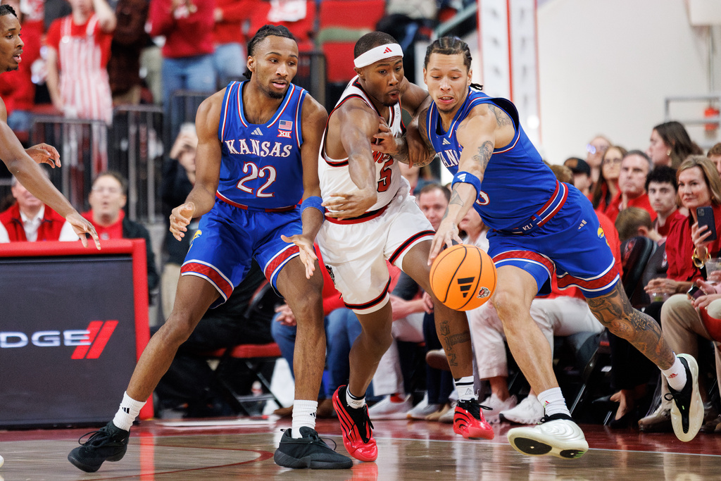 Kansas's Tre White, center, handles the ball ahead of Darryn Peterson (22) as North Carolina State's Tre Holloman, right, defends during the first half of an NCAA college basketball game in Raleigh, N.C., Saturday, Dec. 13, 2025. (AP Photo/Ben McKeown)