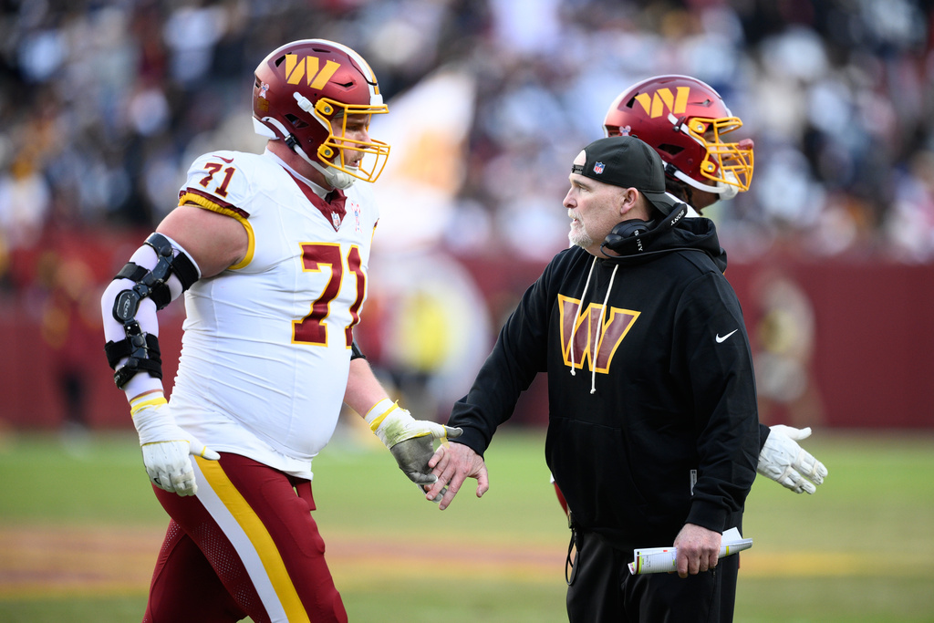 Washington Commanders head coach Dan Quinn shakes hands with Andrew Wylie (71) during the second half an NFL football game Thursday, Dec. 25, 2025, in Landover, Md. (AP Photo/Nick Wass)