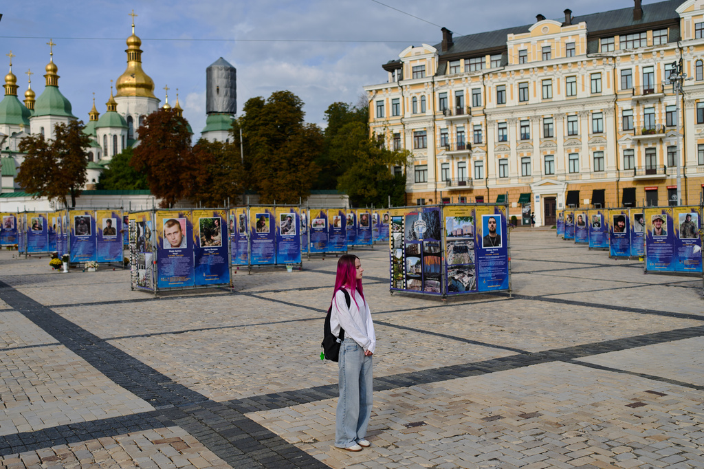 A woman observes a daily nationwide minute of silence in memory of soldiers killed in the war with Russia, some of them with their photos displayed at St. Sophia square in Kyiv, Thursday, Sept. 3, 2026. (AP Photo/Francisco Seco)