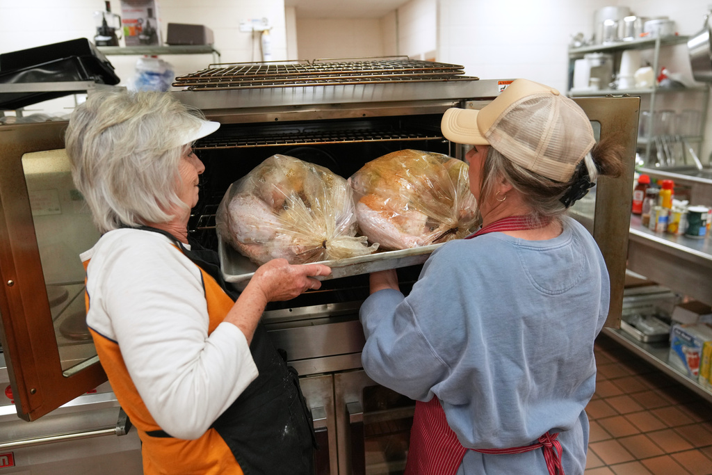 Kristal Porter, right, helps her mother, high school cafeteria worker Shirley Mease, load turkeys into the oven in the kitchen at Reeds Spring High School as they prepare 700 free Thanksgiving meals for community members Wednesday, Nov. 26, 2025, in Reeds Spring, Mo. (AP Photo/Jeff Roberson)