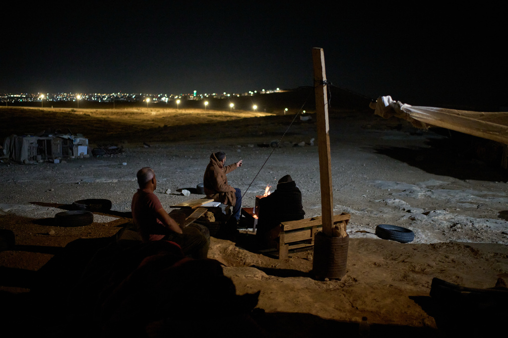 Palestinians sit next to a fire as they take part in a night watch to warn neighbors if Israeli settlers approach their community near the West Bank village of Susya, in the Masafer Yatta region, Thursday, June 18, 2026.. (AP Photo/Leo Correa)