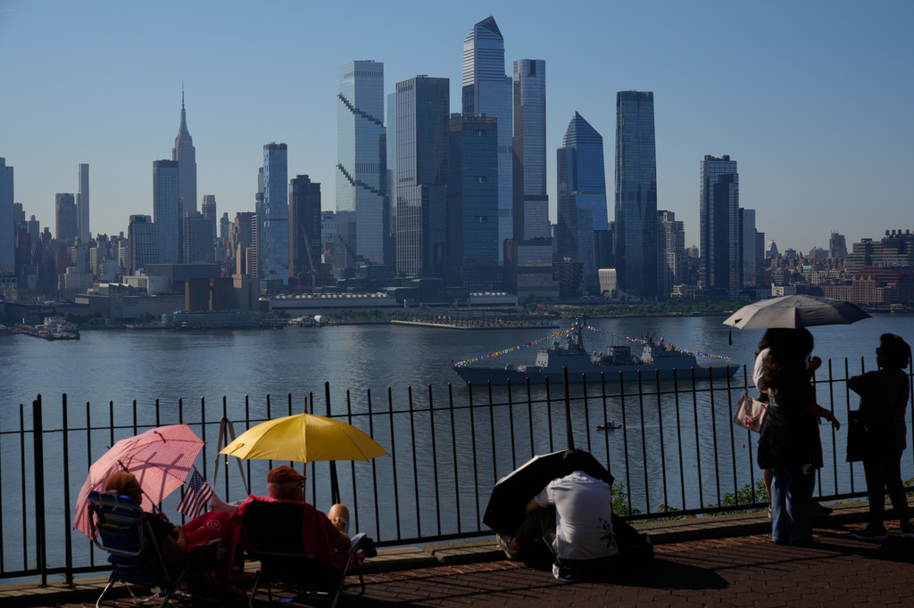 People take cover from the heat under umbrellas as they wait for a parade of tall ships and flyovers in Weehawken, N.J., Saturday, July 4, 2026. (AP Photo/Seth Wenig)