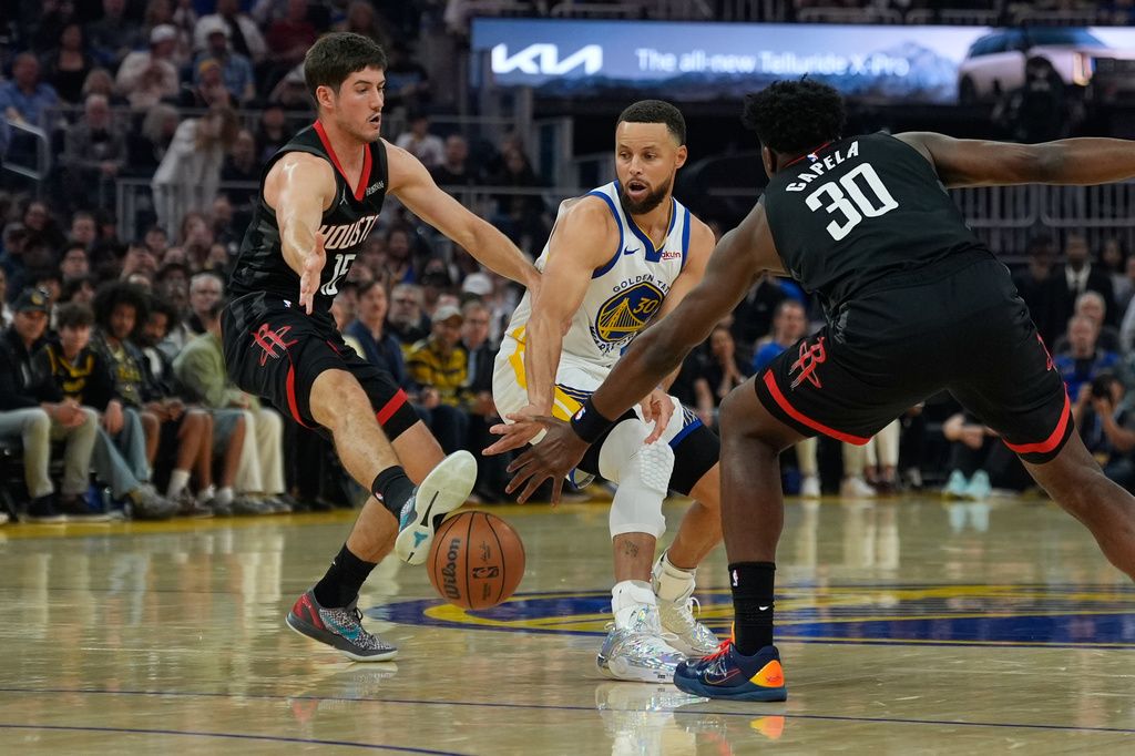 Houston Rockets guard Reed Sheppard, left, kicks a pass by Golden State Warriors guard Stephen Curry, center, during the first half of an NBA basketball game, Sunday, April 5, 2026, in San Francisco. (AP Photo/Godofredo A. Vásquez)