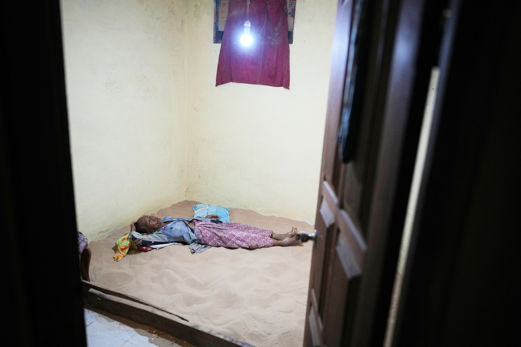 70-year-old Masriani lies on a sand bed in her bedroom in Legung Timur village in Sumenep on Madura Island, Indonesia, Tuesday, Sept. 9, 2025. (AP Photo/Dita Alangkara)